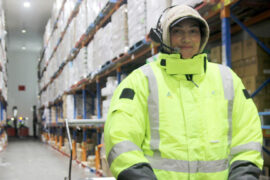 A female warehouse operator wearing a Voice Picking headset and high-visability clothing within an aisle of pallet racking.