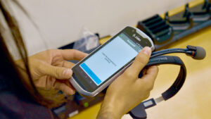 Female hand hold a Voice Picking headset and a Zebra mobile device to complete the simple set up process.